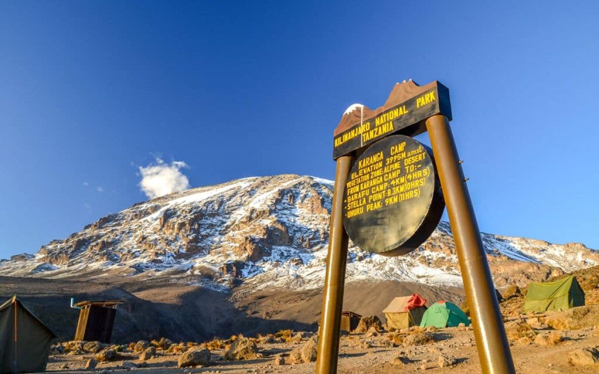 Kilimanjaro, Tanzania - March 9, 2015: Kibo with Uhuru Peak (5895m amsl) at Mount Kilimanjaro, Kilimanjaro National Park, seen from Karanga Camp at 3995m amsl. Park sign and tents in the background.